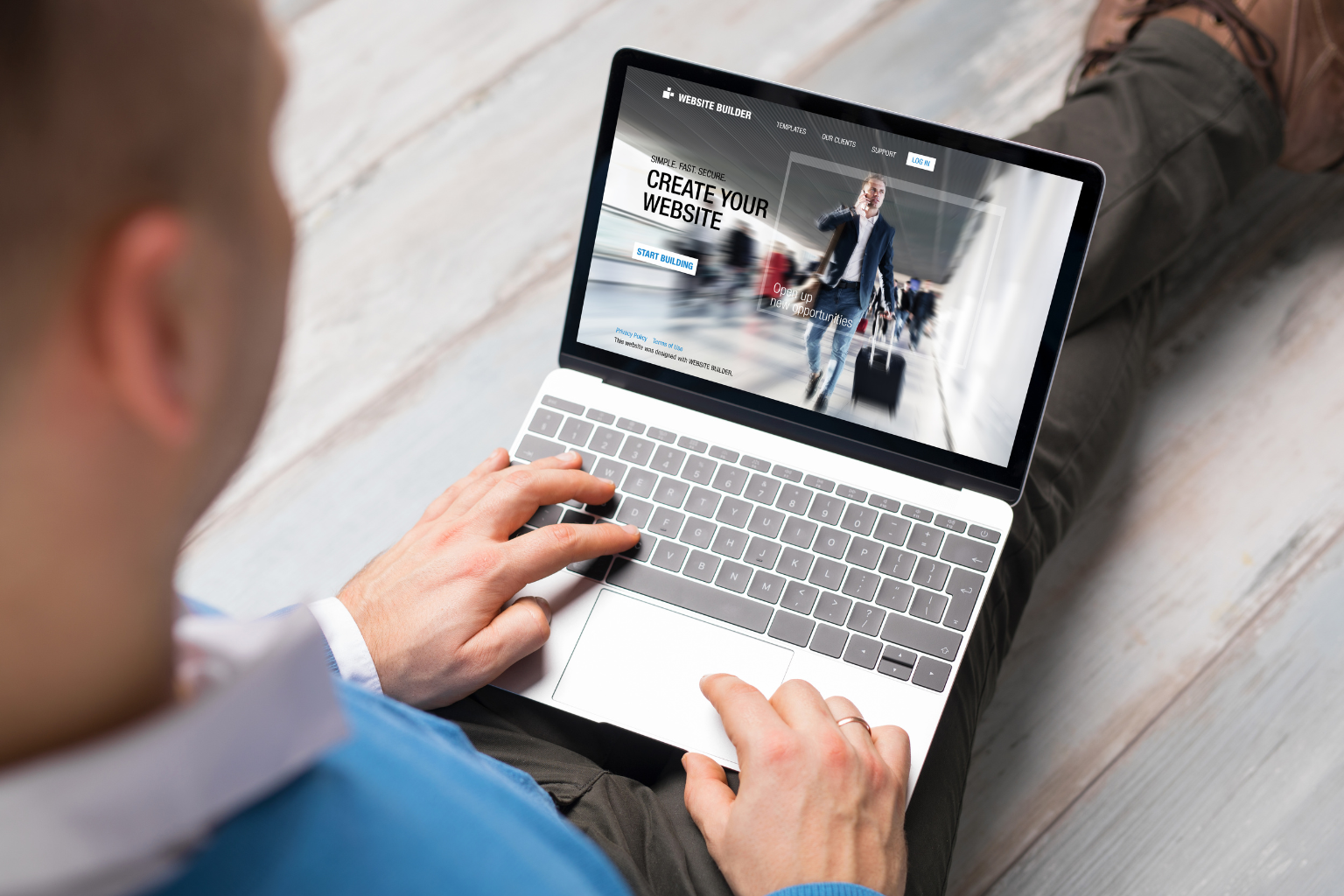 A person in a blue sweater is sitting on the floor using a laptop. The screen displays a Create Your Website page with an image of someone walking with luggage at an airport, providing a step-by-step guide to building a successful courier website.